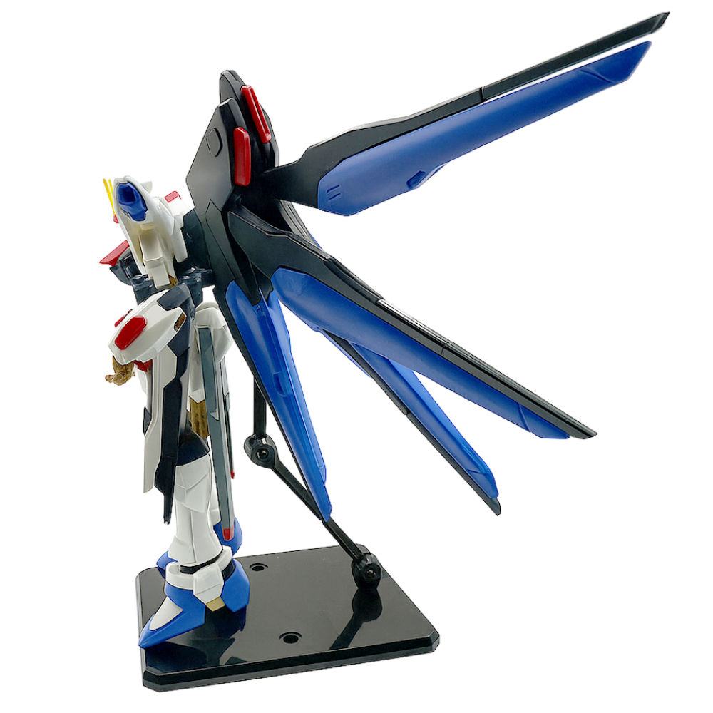 Gundam Strike Freedom figuriini sivulta, siniset siivet avattuna, seisoo mustalla alustalla.