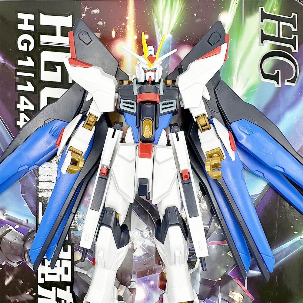 Gundam Strike Freedom figuriini edestä, värikkäällä taustalla tuotepakkauksen grafiikkaa.