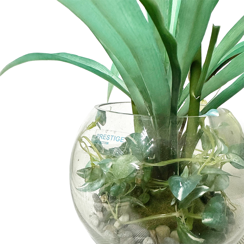 Objet décoratif : arrangement topiaire artificiel dans un vase en verre avec feuillage vert et galets.