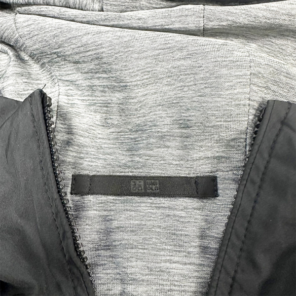 Detalj iznutra Uniqlo reverzibilne parke, sive boje s crnom vanjštinom i vidljivim logom.