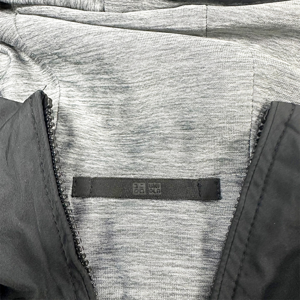 Detalj iznutra Uniqlo reverzibilne parke, sive boje s crnom vanjštinom i vidljivim logom.