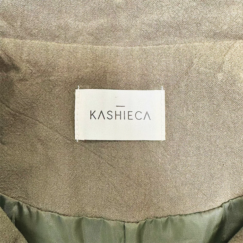 Etiketa z napisom "KASHIECA" na oljčno zeleni obleki.