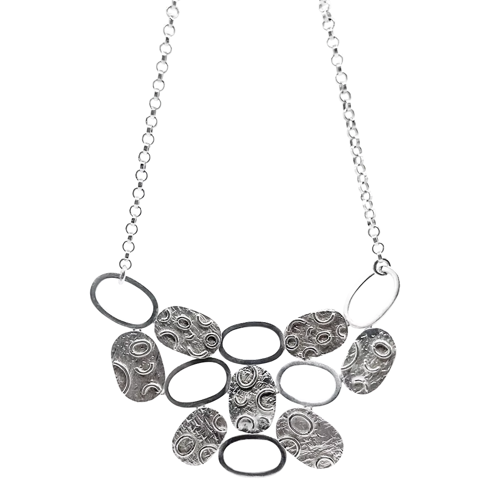 Srebrna ogrlica s krožnimi in ovalnimi obeski z unikatno teksturo, prikazana na beli podlagi.