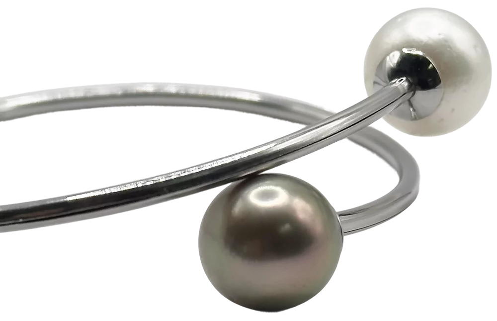 Bracciale in metallo con una perla bianca e una perla nera su estremità opposte.