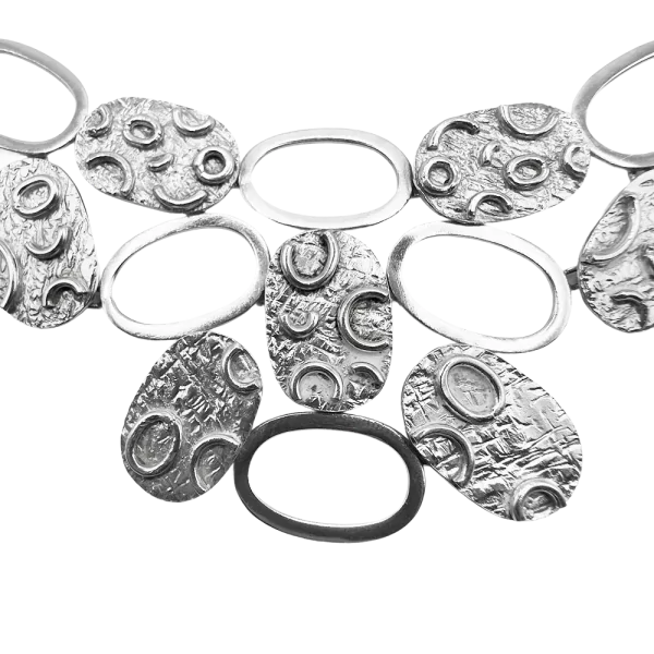 Srebrna ogrlica z ovalnimi diski in teksturiranim vzorcem, razstavljena na belem ozadju.